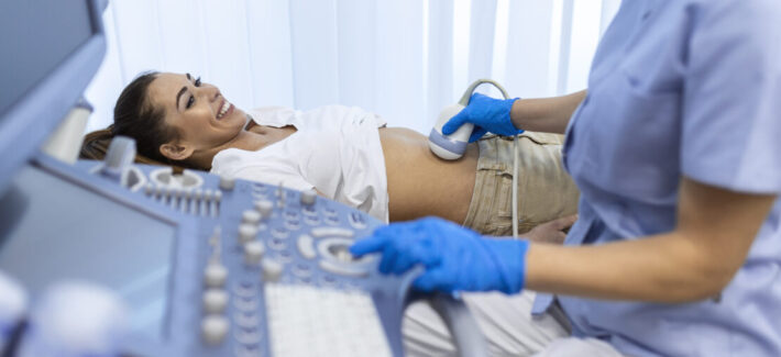 Ultrasound diagnostic of stomach on abdominal to woman in clinic, closeup view. Doctor runs ultrasound sensor over patient's girl tummy and looks at image on screen. Diagnosis of internal organs.